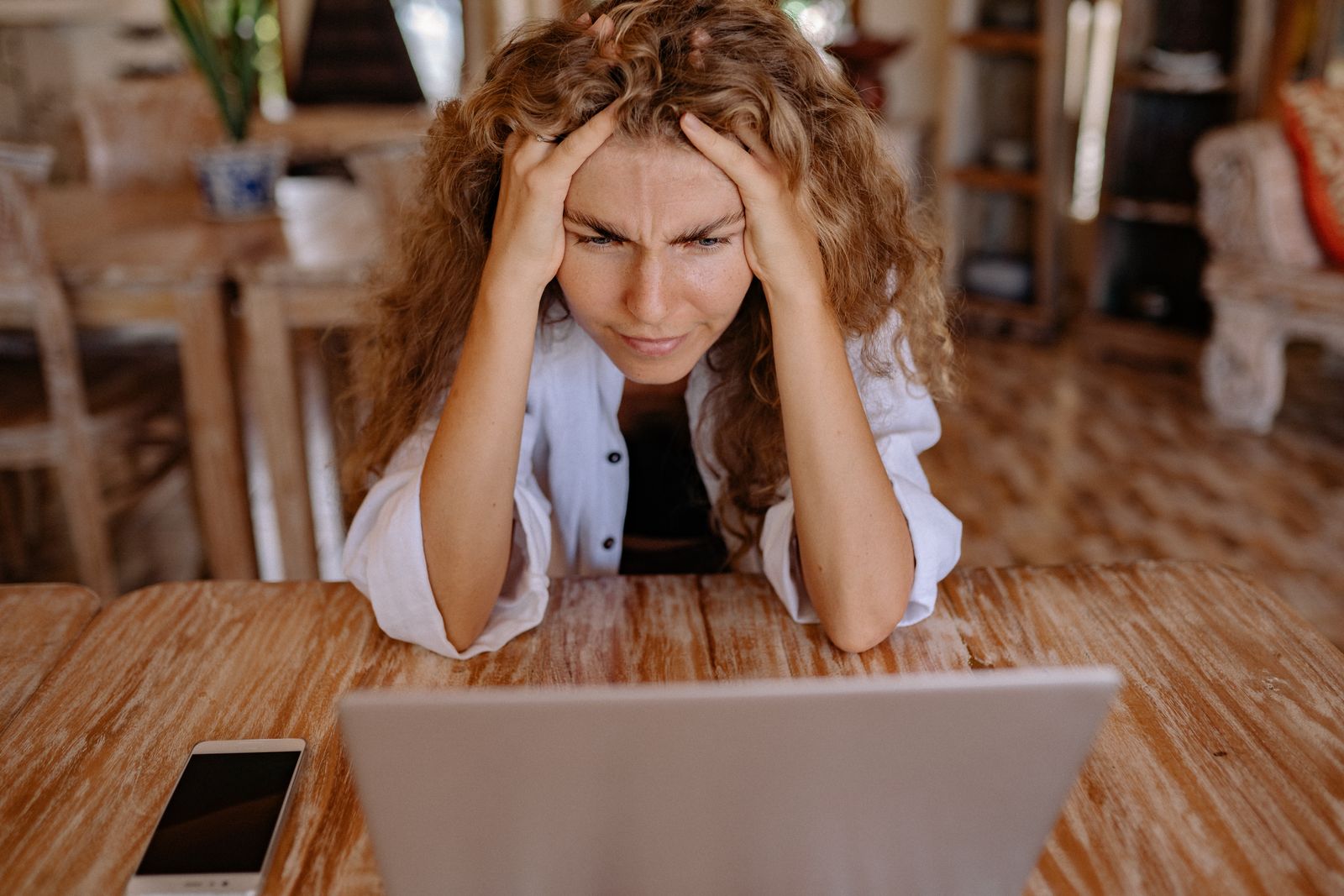 Vrouw aan de keukentafel met de handen in het haar voor haar laptop, telefoon ernaast.